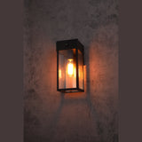 Black framed wall light lit with a warm bulb against a dark wall